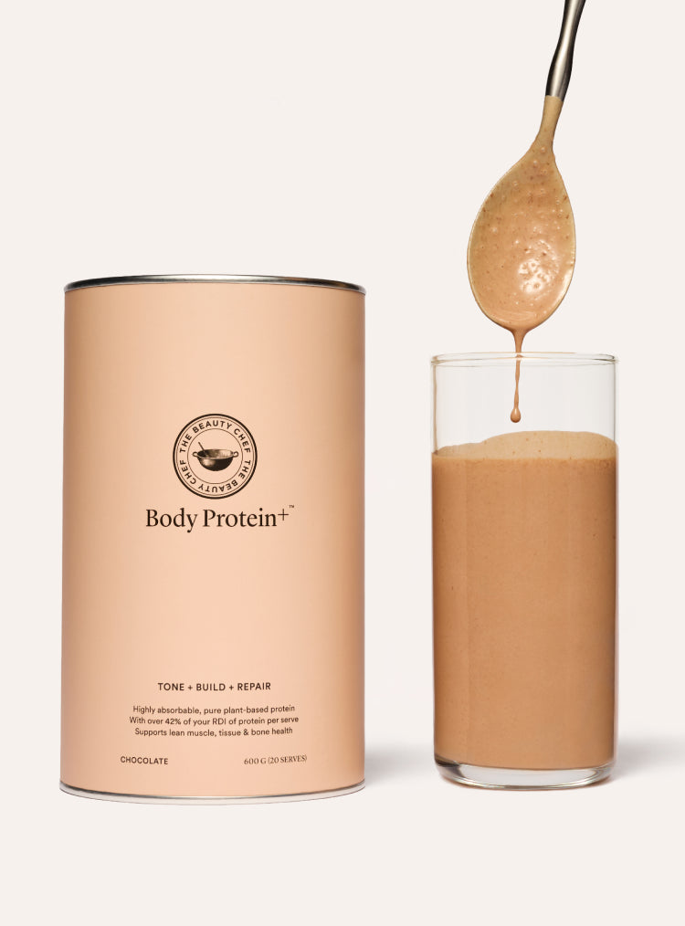The beauty chef Body Protein+ chocolate protein shake with a glass and spoon on a white background