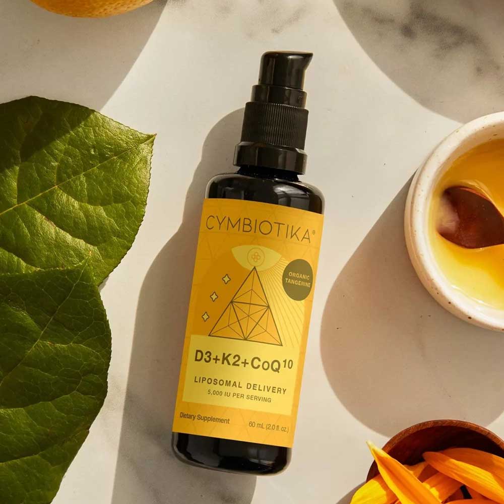 Cymbiotika supplement bottle with a yellow label on a marble surface with leaves and a bowl.