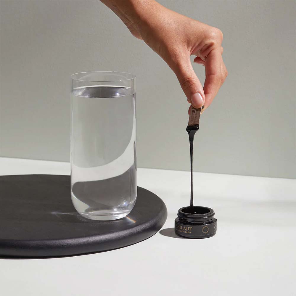 Hand pouring a liquid from a small container into a glass of water on a neutral background