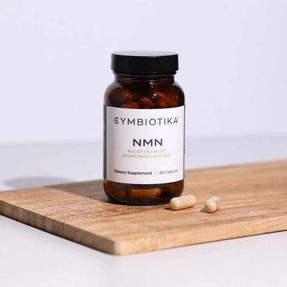 Cymbiotika NMN dietary supplement bottle on a wooden cutting board with a white background