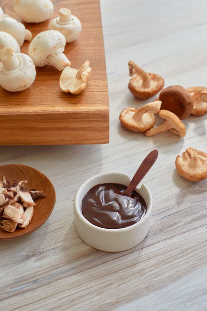 Cymbiotika organic longevity mushrooms on a wooden board with a bowl of chocolate sauce and a spoon.