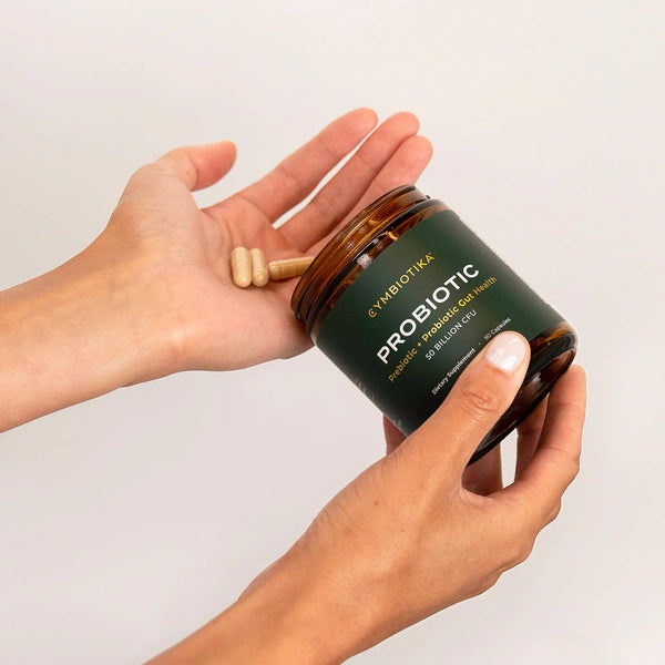 Hand holding a jar of Cymbiotika Probiotic product with a wooden scoop on a light background