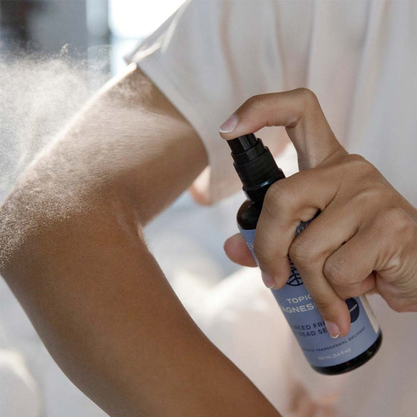 Person using a spray bottle labeled 'Topical Magnesium' on their arm.