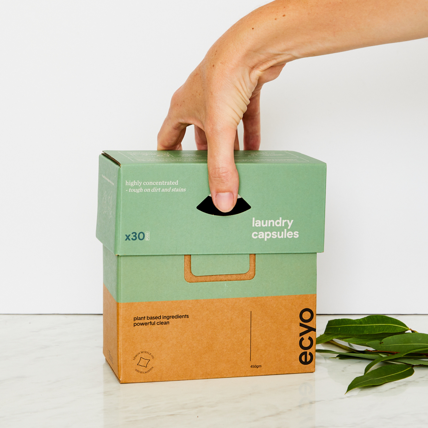Hand holding a box of eco-friendly laundry capsules with a white background