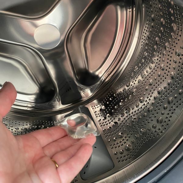 Hand holding a eco laundry capsule in front of opening a washing machine door.