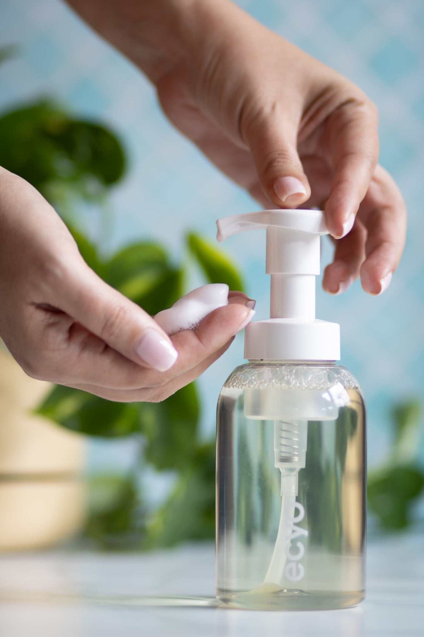 Person using a pump bottle with a blurred green plant background