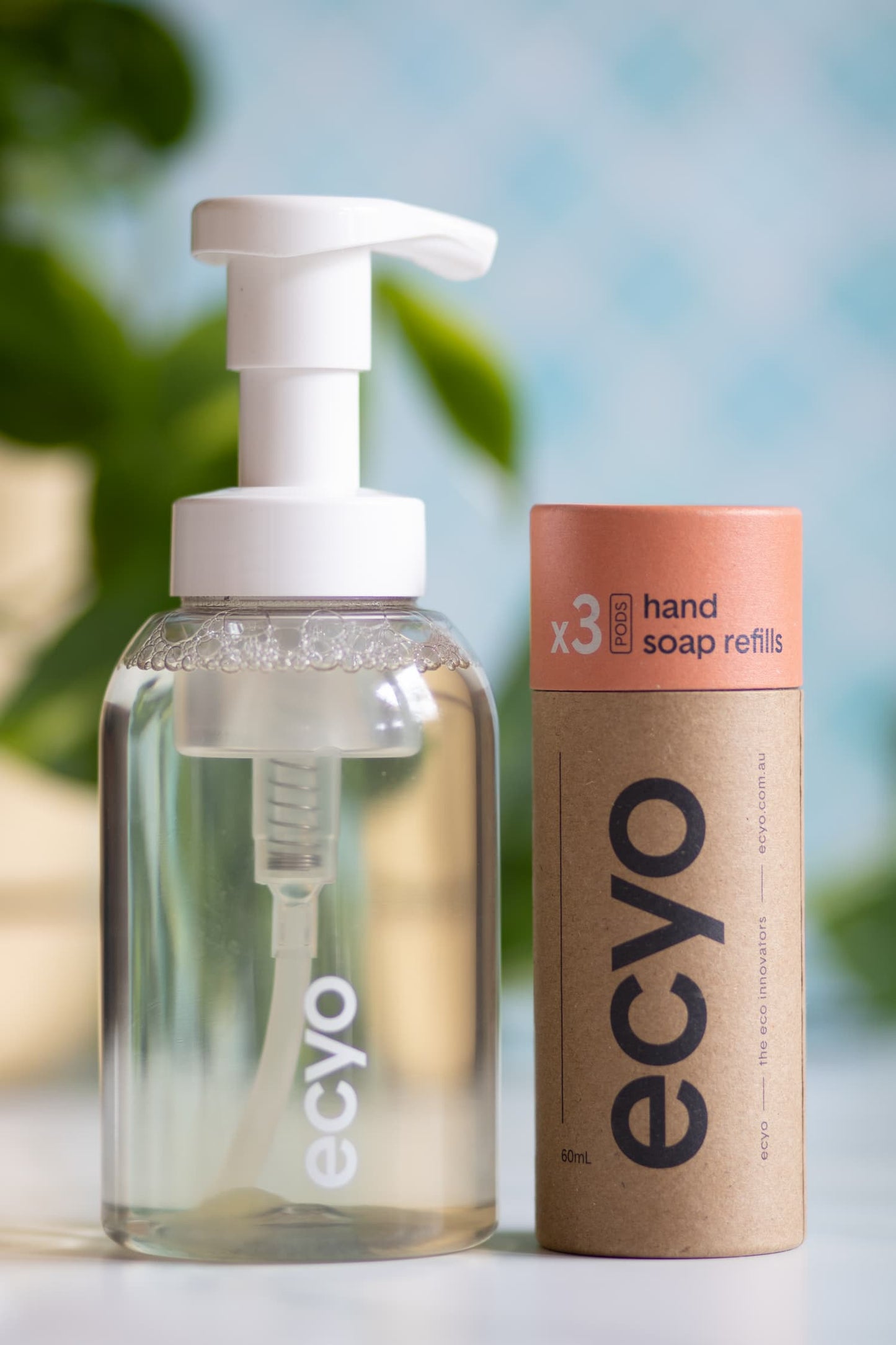 Eco-friendly hand soap bottle and refill container with 'ecyo' branding on a blurred natural background.
