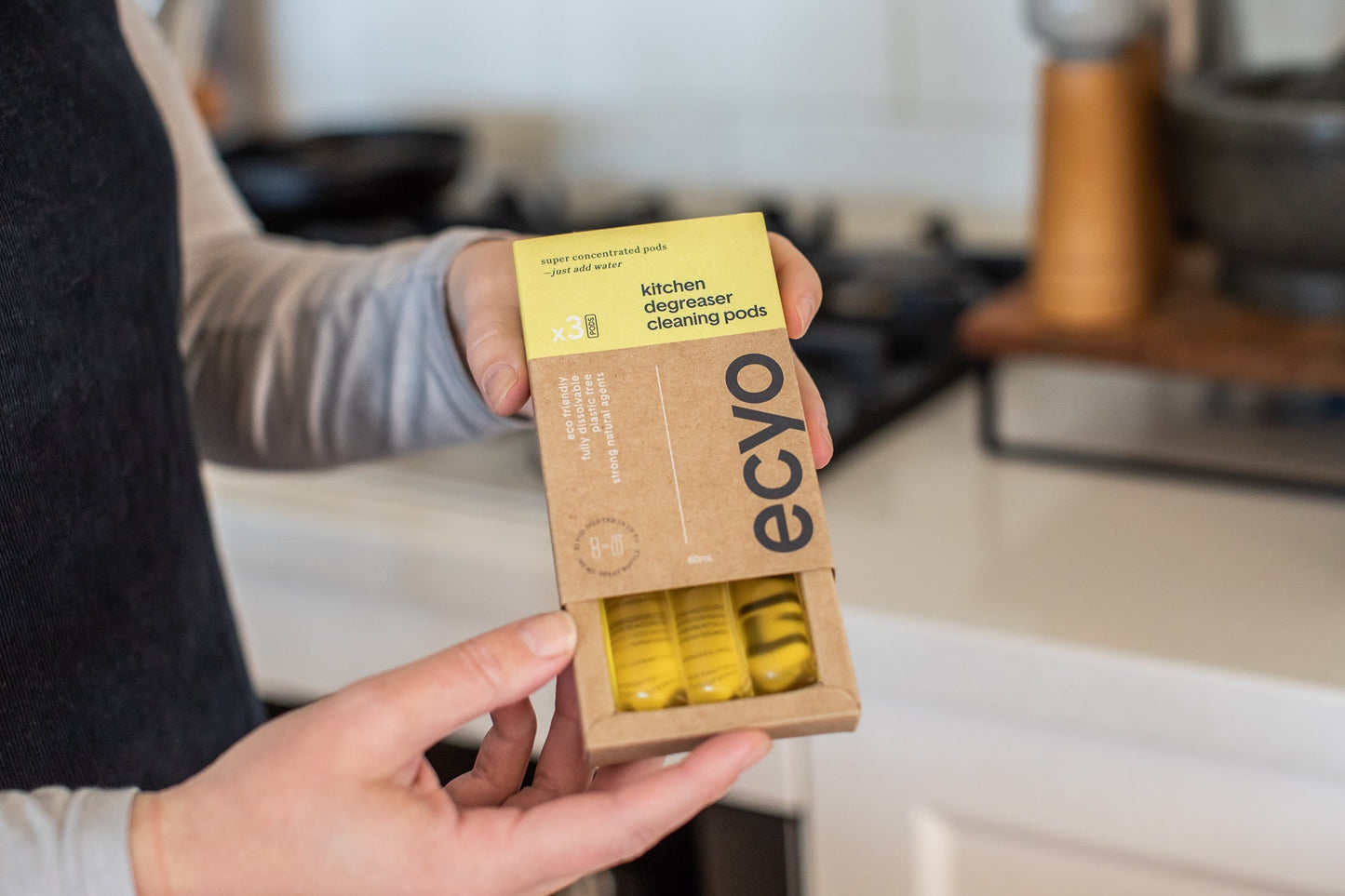 Person holding a box of Ecyo kitchen cleaning pods in a kitchen setting.