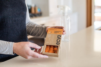 Person holding a box of Ecyo cleaning wipes in a kitchen setting