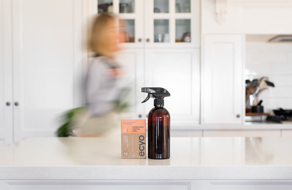 Brown spray bottle and box on a kitchen counter with a blurred person in the background