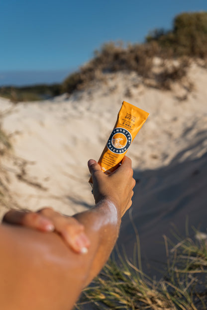 Hand holding a sunbutter sunscreen stick on a sandy beach