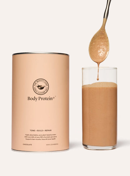 The beauty chef Body Protein+ chocolate protein shake with a glass and spoon on a white background