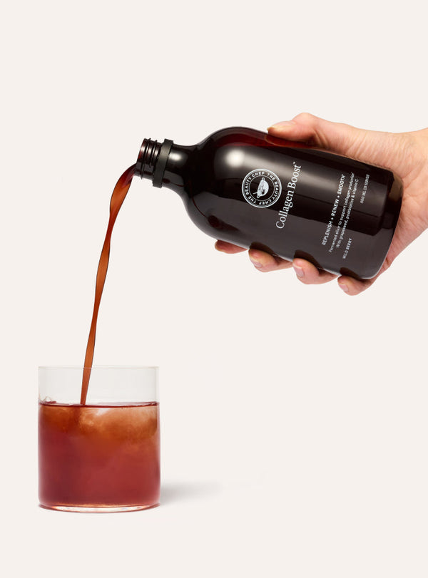 Hand pouring a dark liquid from a bottle labeled 'Collagen boost' into a glass on a white background