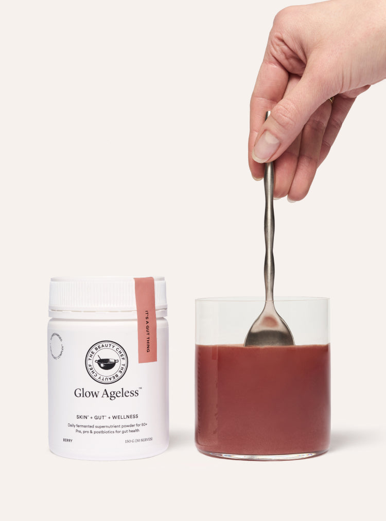 Hand holding a spoon over a jar of red powder with 'Glow Ageless' packaging on a white background