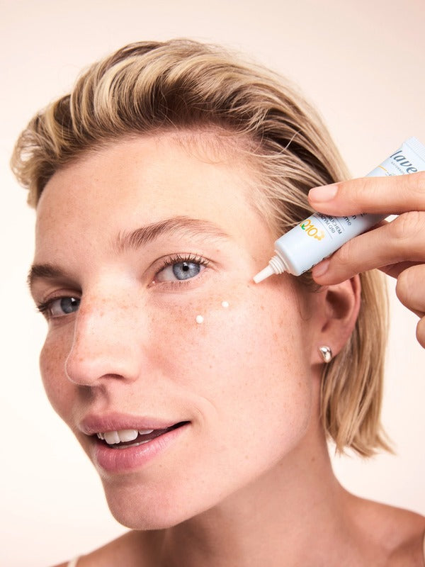 Woman applying small dots of Lavera Basis Sensitiv Q10 Anti-Ageing Eye Cream beneath her eye from the white applicator tube.